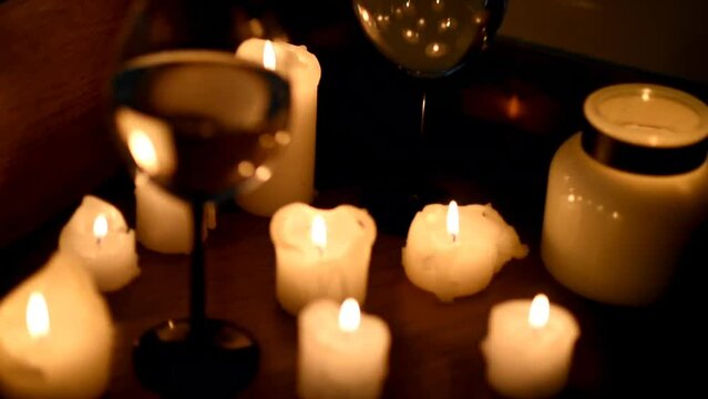 A glass of wine and candles in the dark. The focus shifts from the glass to the candles and the image is blurred in the side. Romantic dinner