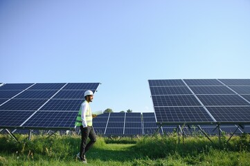 An Indian male engineer in a green vest is working on a field of solar panels. The concept of...