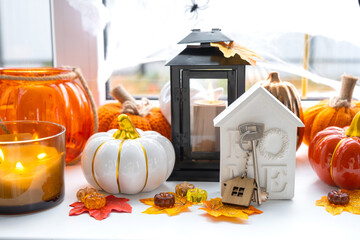 Cozy autumn decor on the windowsill with pumpkins, autumn leaves, a house and keys - autumn mood, Halloween, housing, relocation, mortgage, insurance. - obrazy, fototapety, plakaty