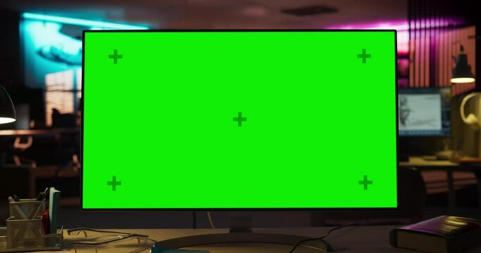 Zoom Out Shot of Desktop Computer Monitor on a Wooden Desk with a Green Screen Chromakey Mock Up Display. Office Working Station for Game Developer in Creative Agency. Template For For Advertising.