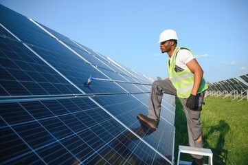 Tidy african american worker is cleaning solar panels with special broom.