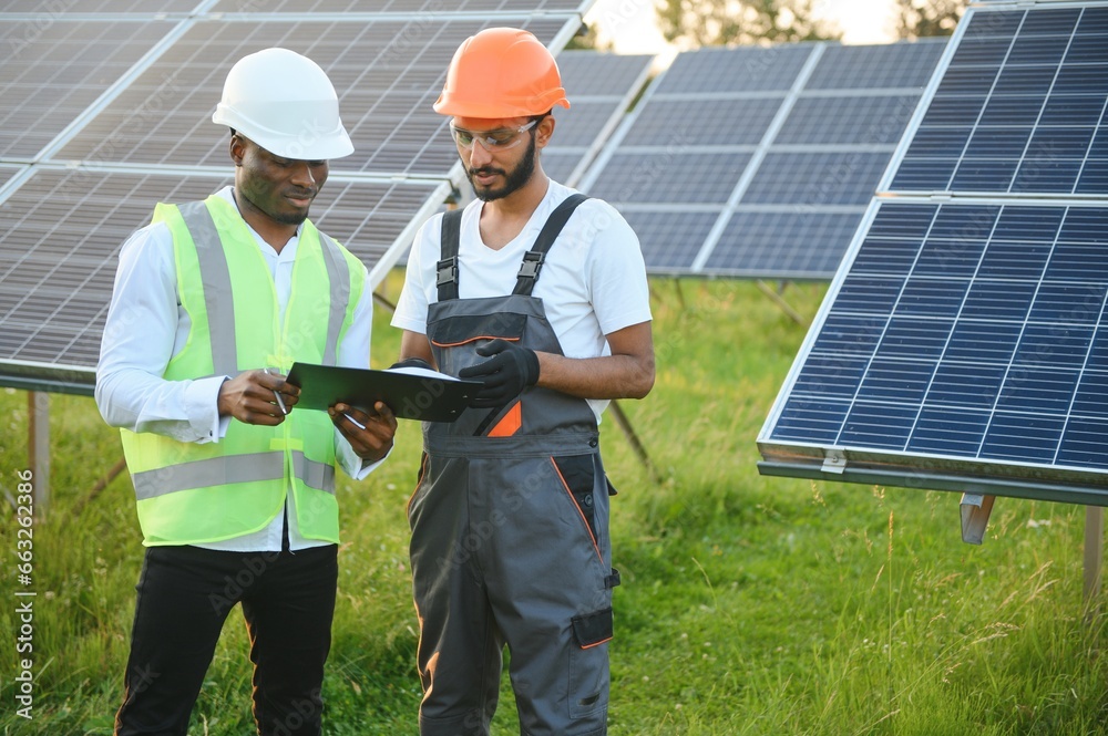 Wall mural Multiracial team of engineers on solar panels. African american and arab engineer working on solar panel farm.