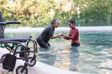 Fototapeta premium Selective focus off wheelchair background of physical therapist helping senior woman in aqua, old women and mature doing aqua aerobics exercise in swimming pool, Elderly sports, and active lifestyle.