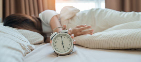 alarm clock and asian woman hand stop time in bed while sleeping, young adult female wake up late in the early morning. Relaxing , sleepy, daily routine and have a nice day concepts