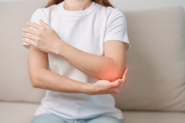 Woman having elbow ache during sitting on couch at home, muscle pain due to lateral epicondylitis or tennis elbow. injury, Health and medical concept - obrazy, fototapety, plakaty