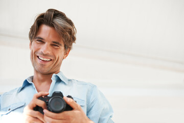 Smile, camera and young man photographer at a photoshoot for creative work project. Happy, photography and portrait of handsome male person with dslr device for art career by white studio background.