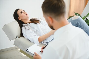 Fototapeta premium Psychologist taking notes during therapy session with sad young woman in his office. Copy space