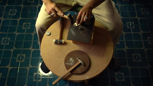 Man hammering brass sheet in goldsmith workshop.