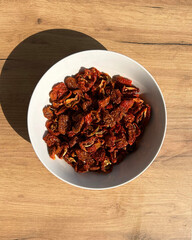 Bowl of dried tomatoes on wooden background, top view