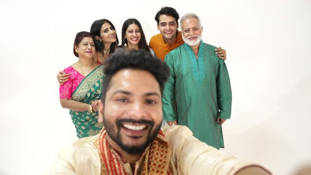 Indian happy family take A selfie picture on mobile, while standing together against white background.they all are very happy,wearing traditional dress.