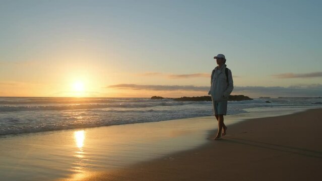 Happy young man walking on a sandy ocean beach on a sunny summer day, in slow motion. Young Male guy walking along the sandy coast on a sunny evening. A guy with a backpack walks on a beach