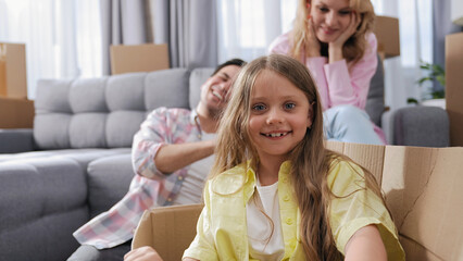 Cute little girl sit inside carton box. Family move into house. Nice kid look at camera. Happy child portrait. Buyer rent home. Tenant buy real estate concept. Fun joy face smile. People bought flat.
