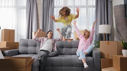Happy family move into new house. Little girl jump on sofa. Crazy child have fun. Funny dad buy...