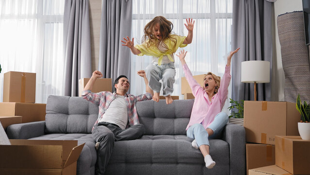 Happy family move into new house. Little girl jump on sofa. Crazy child have fun. Funny dad buy flat. Silly kid play home. Joy mom rest couch. Sale real estate concept. Smiling people rent furniture.