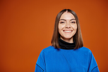 attractive smiley woman in casual blue jacket smiling cheerfully at camera on orange background