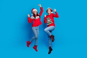Fototapeta na wymiar Full length photo of cheerful lucky ladies santa helpers dressed print sweaters jumping high celebrating xmas isolated blue color background
