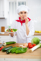 Female chef in white uniform showing approving gesture satisfied with vegetable salad