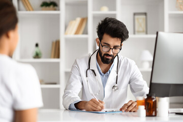 Young indian man doctor consulting woman patient at clinic - obrazy, fototapety, plakaty