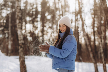 a young woman in a winter park holds snow in her hands