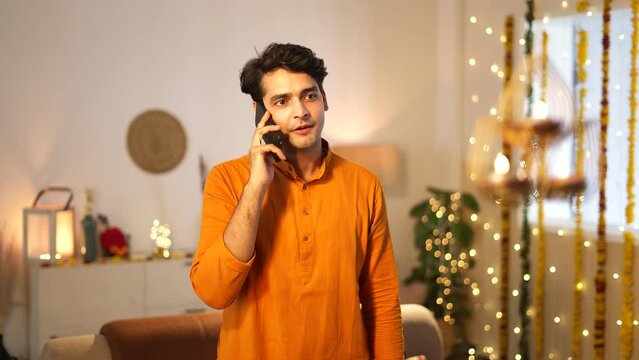 Indian handsome man wearing traditional clothes talking on the phone during diwali celebration.he is standing against decorated background,festival concept