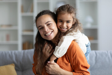 Family bonding. Portrait of happy mother and her cute daughter sharing warm embrace and smiling to...