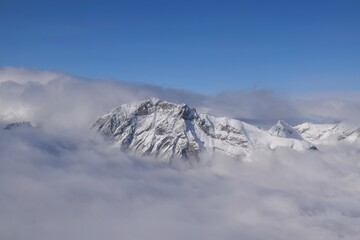 Fototapeta na wymiar Breathtaking aerial view of alpine snowcapped mountain range peaking through heavy clouds. Mountain peaks of the Ötztal Alps from above. The impressive winter view is taken from an airplane window.