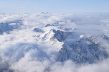 Breathtaking aerial view of alpine snowcapped mountain range peaking through heavy clouds. Mountain...