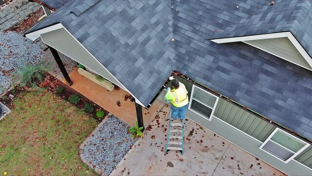 Worker is cleaning clogged roof gutter from dirt, debris fallen leaves to prevent water let rainwater drain