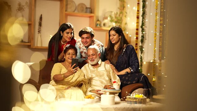 Cheerful Indian parents and their son,wife waving their hands while talking on a video call - a celebration time. Happy family celebrating the festival of Diwali together.connectivity concept.