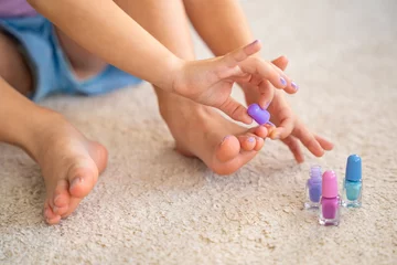 Photo sur Plexiglas Pédicure Close up view of hands of little girl doing pedicure and painting nails with colorful pink, blue and purple nail polish at home living room