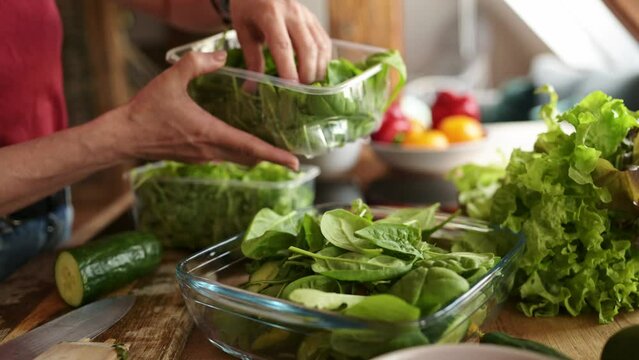 woman adding a spinach leaves to the salad in the kitchen