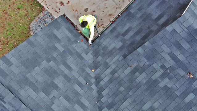 Worker is cleaning dirt, debris, fallen leaves from roof gutter drain that has become clogged