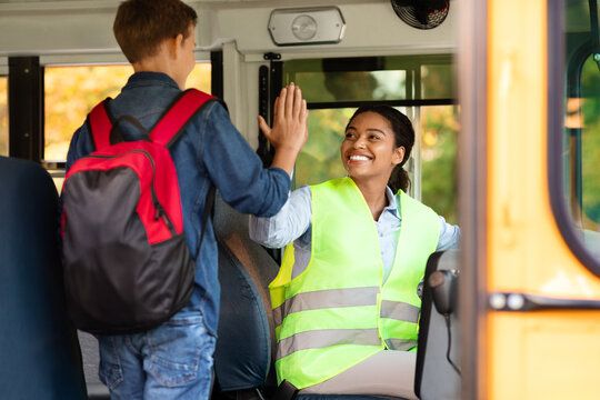 Smiling school bus female driver giving high five to cheerful little girl