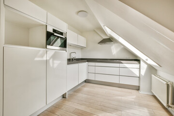 an attic kitchen with white cabinets and wood flooring in the center of the room, there is a microwave on the wall
