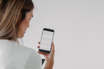 Back side view of asian woman holding smartphone, showing empty white screen phone, isolated over white background wall.