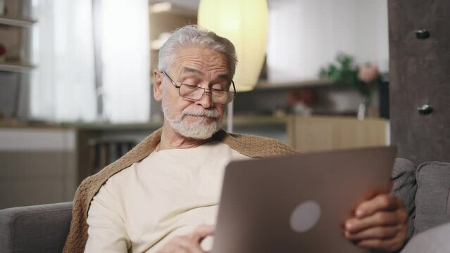 Sad grey haired senior man or freelancer with lack of new ideas or creative block typing and deleting text on laptop computer at home Worried male changing mind every few seconds indoors