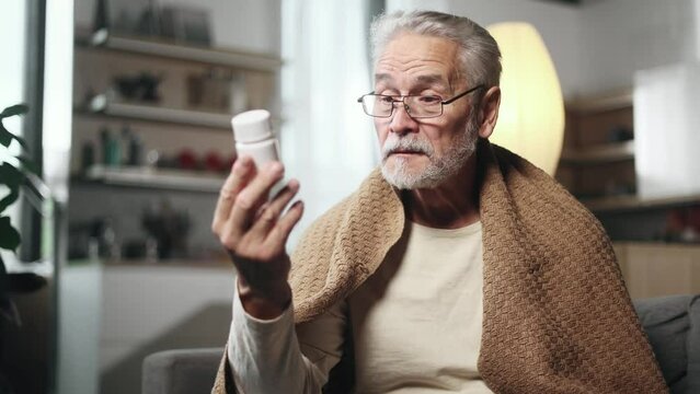 Smiling grey haired senior man reading medical instructions or composition of drug before taking medicine at home Satisfied mature male checking pills for ingredients information and like it indoors