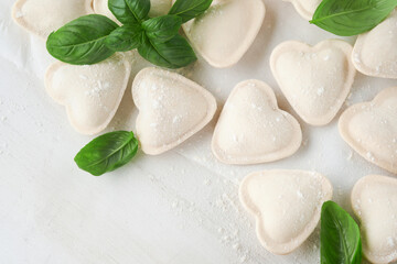 Fototapeta na wymiar Italian ravioli pasta in heart shape. Tasty raw ravioli with flour and basil on white background. Food cooking ingredients background. Valentines or Mothers Day lunch ideas. Top view with copy space.