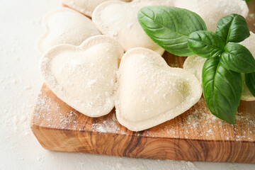 Italian ravioli pasta in heart shape. Tasty raw ravioli with flour and basil on white background. Food cooking ingredients background. Valentines or Mothers Day lunch ideas. Top view with copy space.