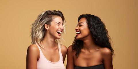 Portrait of two young women of different races laughing and having fun together on a beige background