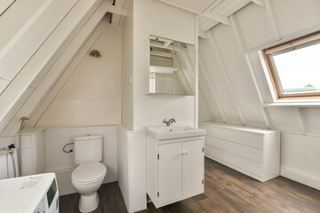 a bathroom in a small room with wood flooring and white walls, there is a mirror on the wall
