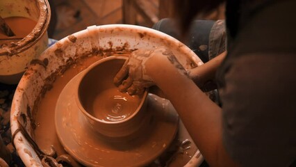 Young woman working on a potter's wheel, exploring the clay sculpting and handmade pottery process, wheel throwing workshop, high quality cinematic 4K slowmotion relaxation hobby concept footage.