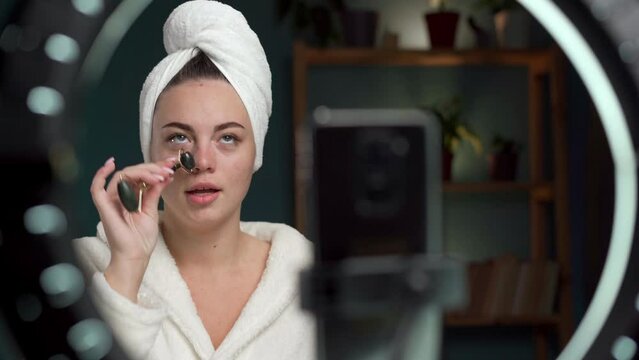 Blogging modern skin care and beauty concept. Cute woman in towel records video tutorial at home using a natural face roller shoots broadcast live video to social network.