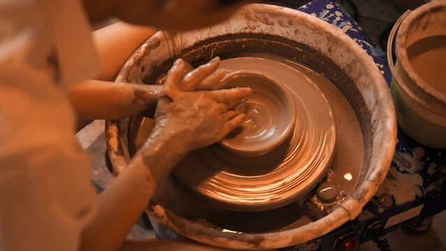 Young woman working on a potter's wheel, exploring the clay sculpting and handmade pottery process, wheel throwing workshop, high quality cinematic 4K slowmotion relaxation hobby concept footage.