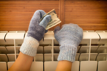 Hands in warm knitted mittens warm themselves on the radiator.