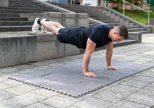 Young man doing a decline push-up or elevated push-up on concrete background outdoors - Powered by Adobe