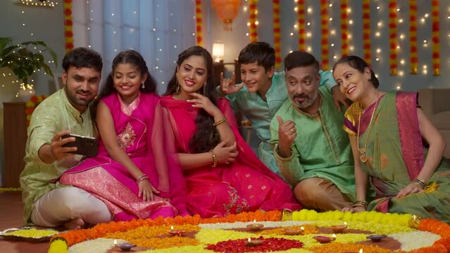 Group of Indian joint family members taking selife in front of decorated diwali rangoli at home - concept of festival gathering, reunion and festival celebration