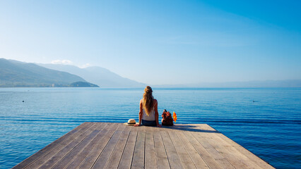 Woman sitting on wooden pier at Ohrid lake shore in Macedonia- tour tourism,travel destination,vacation concept