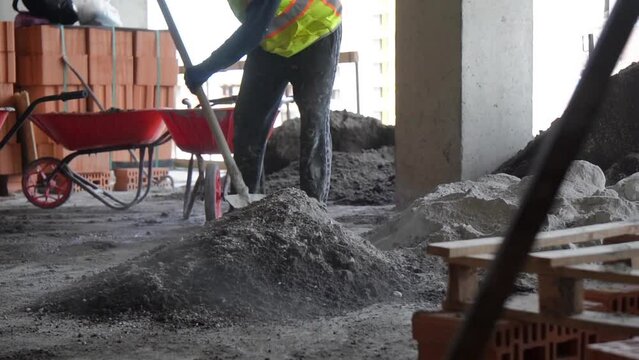 An unrecognizable construction worker mixes cement with shovel at construction site in slow motion. Hard physical work concept.