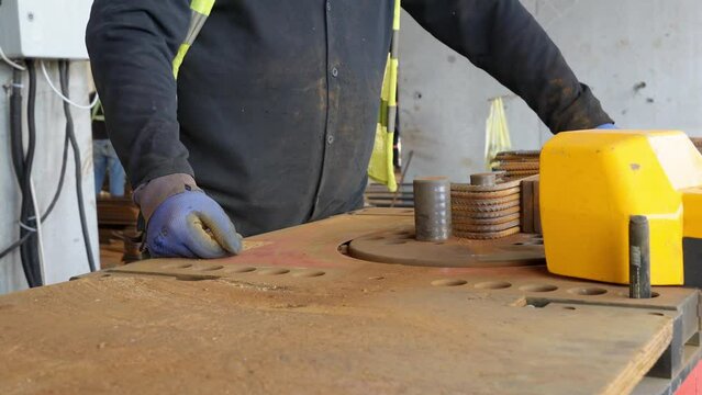A worker prepares reinforcement, showcasing the hands-on process of bending metal on specialized machinery. Close-up on skilled hands in action.